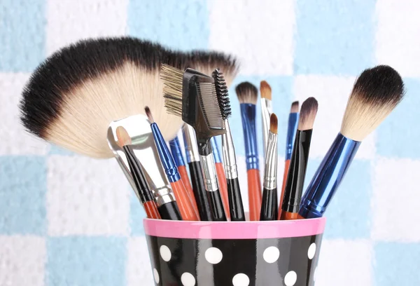 Pincéis de maquiagem em uma xícara preta de bolinhas no fundo colorido close-up — Fotografia de Stock
