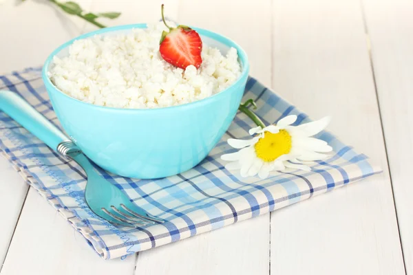 Fromage cottage avec fraise dans un bol bleu et fourchette sur serviette à carreaux bleu sur table en bois blanc close-up — Photo