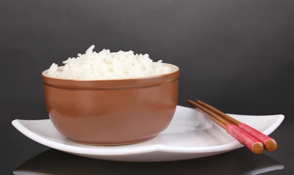 Tigela de arroz e pauzinhos no prato em fundo cinza — Fotografia de Stock