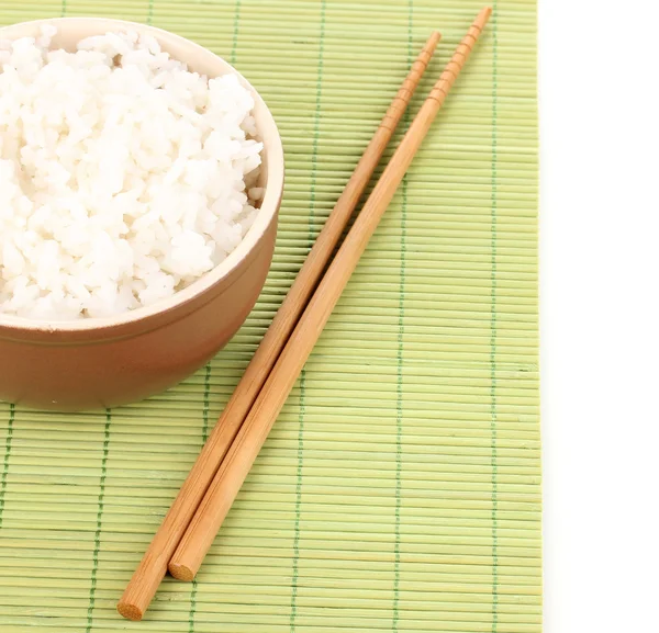 Чаша риса и палочки для еды на бамбуковом коврике, изолированном на белом — стоковое фото