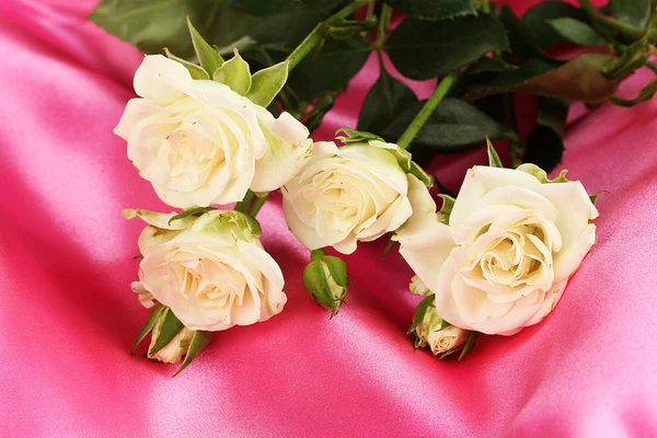 Красивые белые розы на розовом атласе крупным планом — стоковое фото