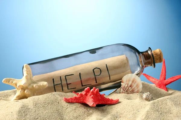 Skleněná láhev s poznámkou uvnitř na písku, na modrém pozadí — Stock fotografie