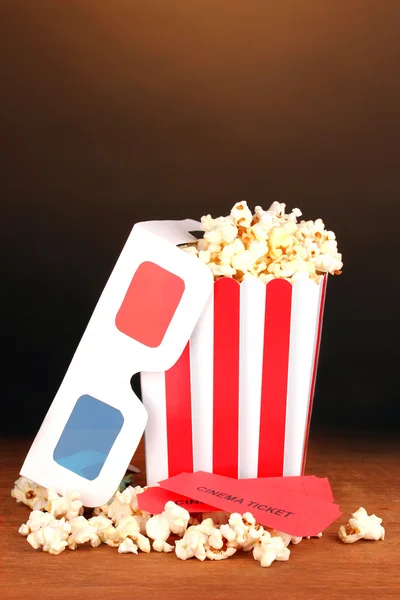 Popcorn with tickets and cinema glasses on wooden table on brown background — Stock Photo, Image