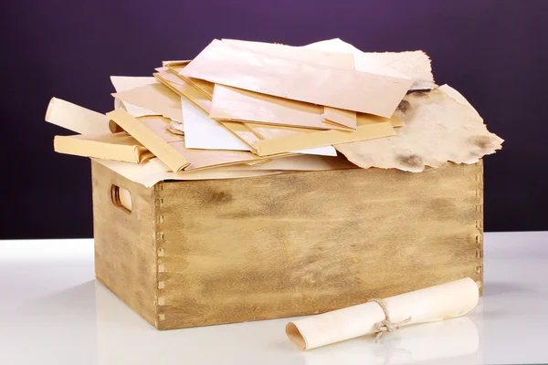 Caixa de madeira com papéis e letras sobre fundo roxo — Fotografia de Stock