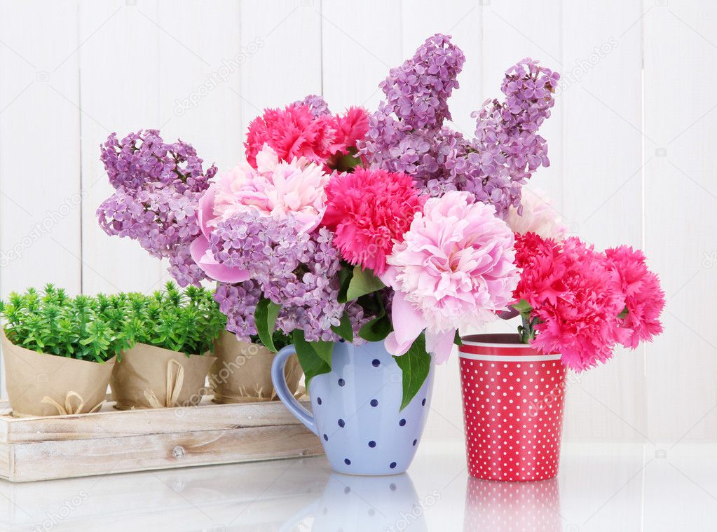 Spring flowers in cups on table on white wooden background