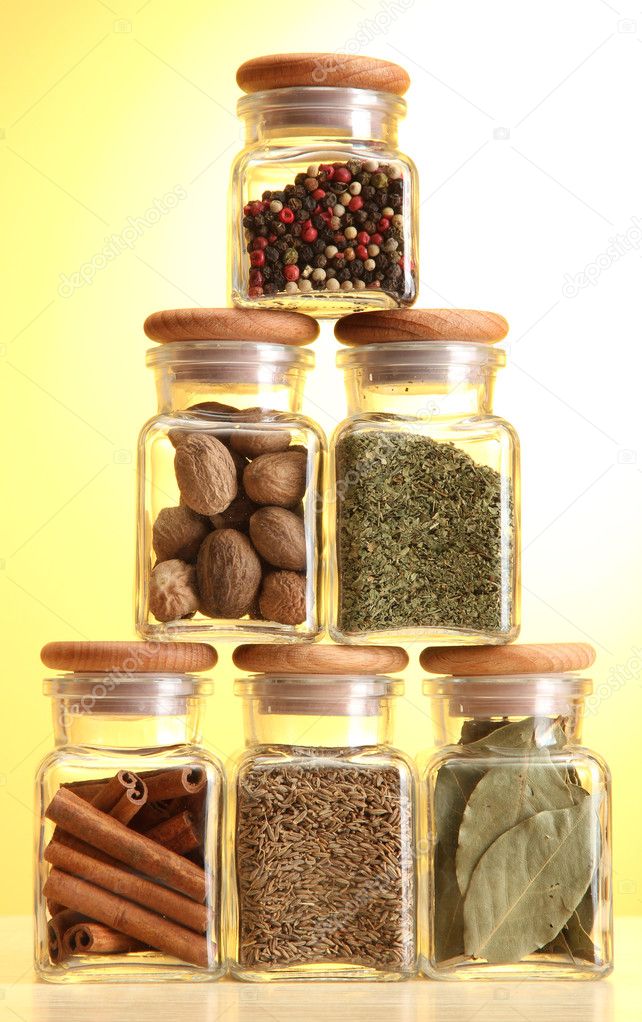 Powder spices in glass jars on yellow background