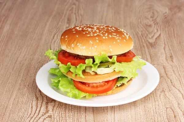 Stor och välsmakande hamburgare på plattan på träbord — Stockfoto
