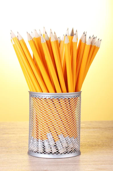 Crayons de plomb dans une tasse en métal sur une table en bois sur fond jaune — Photo