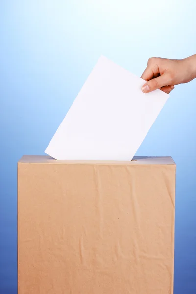 Hand with voting ballot and box on blue background — Stock Photo, Image