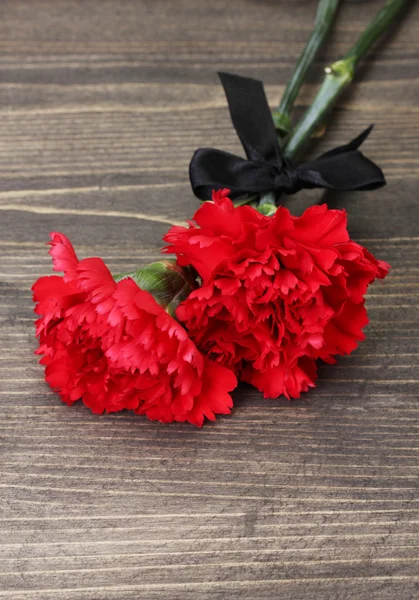 Carnations and black ribbon on grey wooden background — Stock Photo, Image
