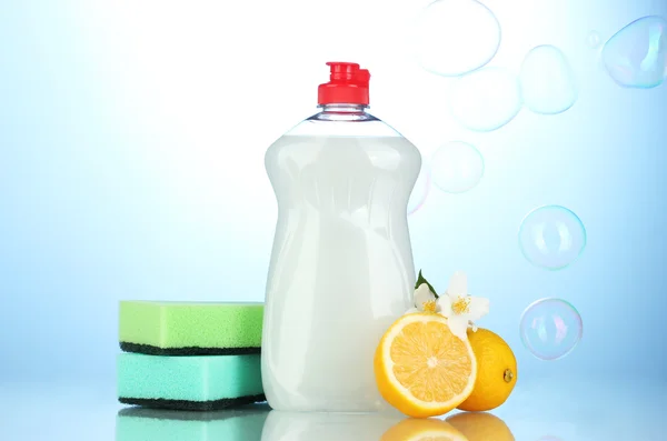 Liquido per lavastoviglie con spugne e limone con fiori su sfondo blu — Foto Stock