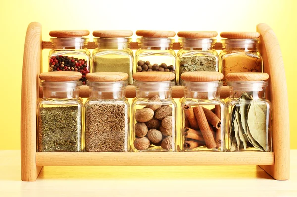 Powder spices in glass jars on wooden shelf on yellow background — Stock Photo, Image