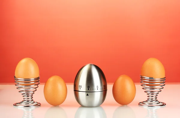 Egg timer and eggs on red background — Stock Photo, Image