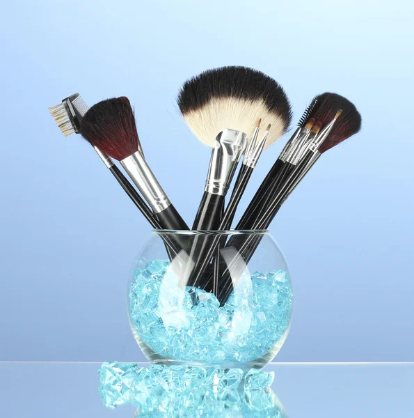 Cepillos de maquillaje en un tazón con piedras sobre fondo azul —  Fotos de Stock