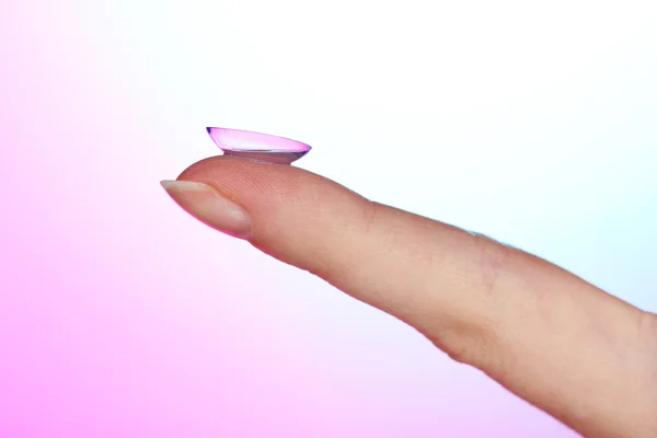 Lente de contato no dedo no fundo azul-rosa — Fotografia de Stock