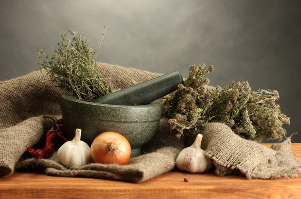 Erbe essiccate in mortaio e verdure, su tavola di legno su fondo grigio — Foto Stock
