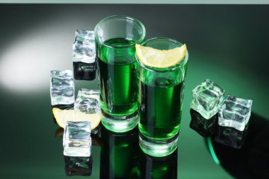 Two glasses of absinthe, lemon and ice on green background clipart