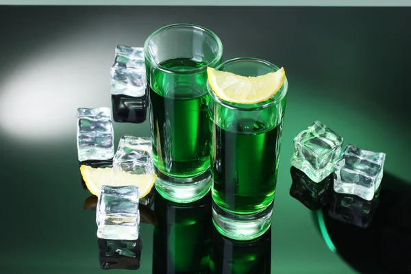 Dois copos de absinto, limão e gelo no fundo verde — Fotografia de Stock