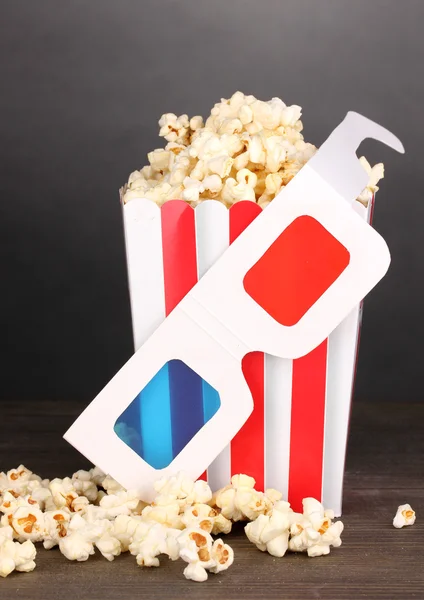 Popcorn a kino brýle na dřevěný stůl na šedém pozadí — Stock fotografie