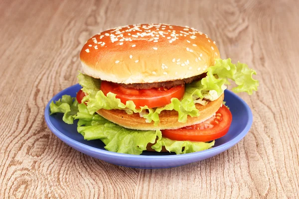 Большой и вкусный гамбургер на тарелке на деревянном столе — стоковое фото