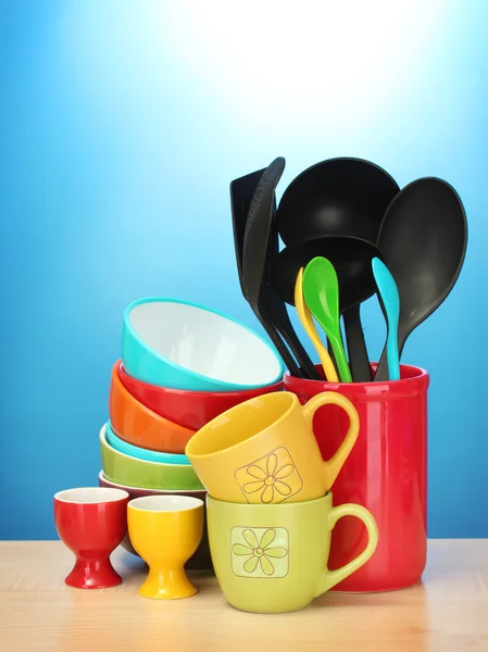Tigelas vazias brilhantes, copos e utensílios de cozinha na mesa de madeira no fundo azul — Fotografia de Stock
