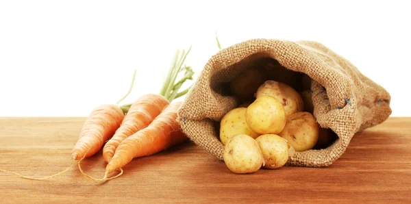 Las patatas jóvenes en el saco con la zanahoria a la mesa sobre el fondo blanco el primer plano —  Fotos de Stock
