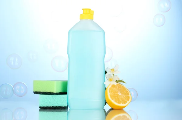 Płyn do mycia naczyń z gąbki i cytryny z kwiatami na niebieskim tle — Zdjęcie stockowe