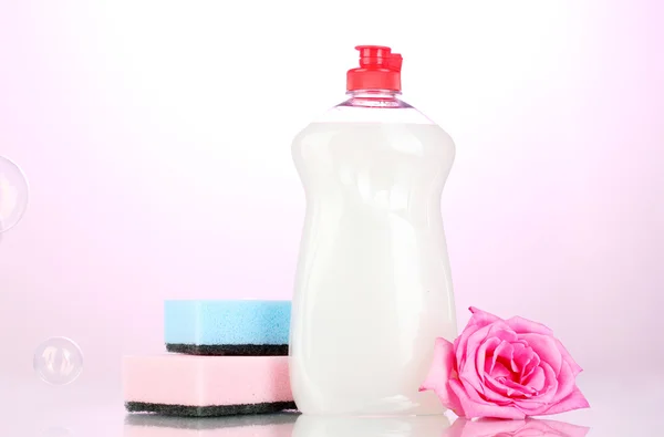Dishwashing liquid with sponges and flower on pink background — Stock Photo, Image