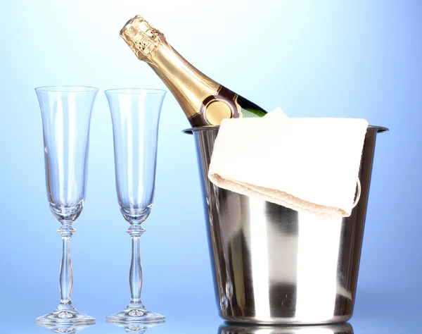 Láhev šampaňského v kbelík s ledem a brýle na modrém pozadí — Stock fotografie