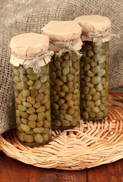 Glass jars with tinned capers on sack background close-up — Stock Photo, Image