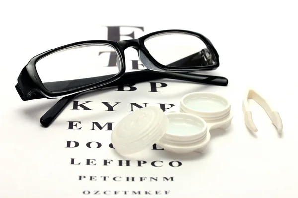 Glasses, contact lenses in containers and tweezers, on snellen eye chart background — Stock Photo, Image