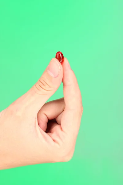 Woman's hand holding a red pill on green background close-up Royalty Free Stock Images
