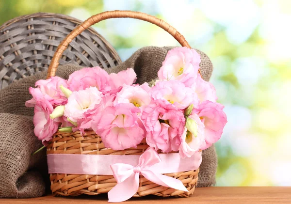 Bouquet of eustoma flowers in basket, on wooden table, on green background — Stock Photo, Image