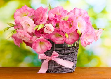 Bouquet of eustoma flowers in wicker vase, on wooden table, on green background clipart