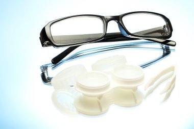 Glasses, contact lenses in containers and tweezers on blue background clipart