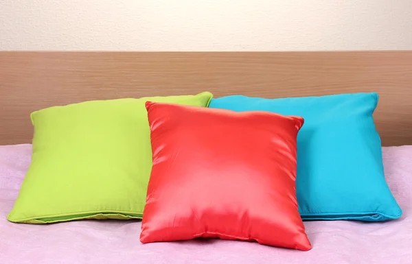 Jasne poduszki na łóżku na beżowym tle — Zdjęcie stockowe