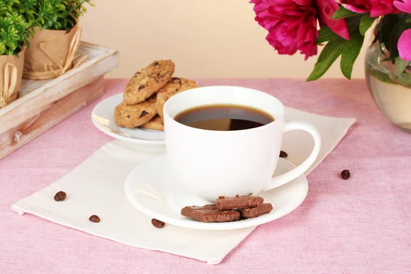 Šálek kávy, sušenky, čokolády a květiny na stole v kavárně — Stock fotografie