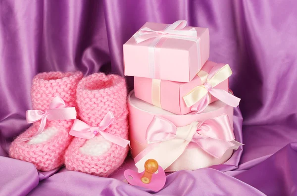 Růžové dětské boty, dudlík, dary na hedvábné pozadí — Stock fotografie