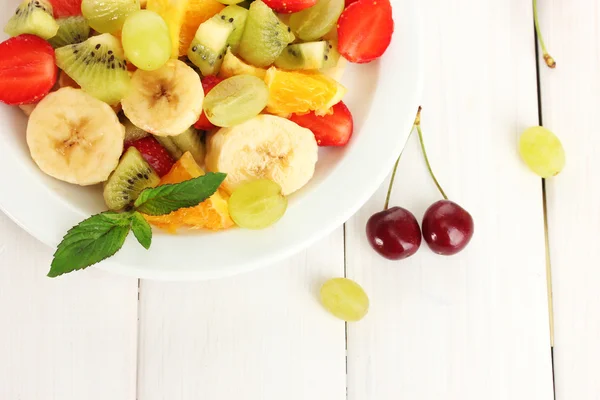 Ensalada de frutas frescas en plato y bayas en mesa de madera blanca —  Fotos de Stock
