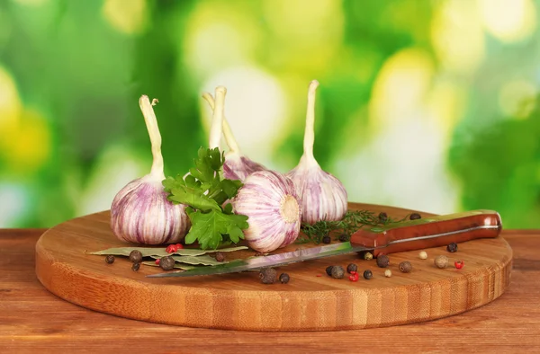 Alho jovem na tábua de corte com vegetação, pimenta e faca na mesa de madeira no fundo verde — Fotografia de Stock