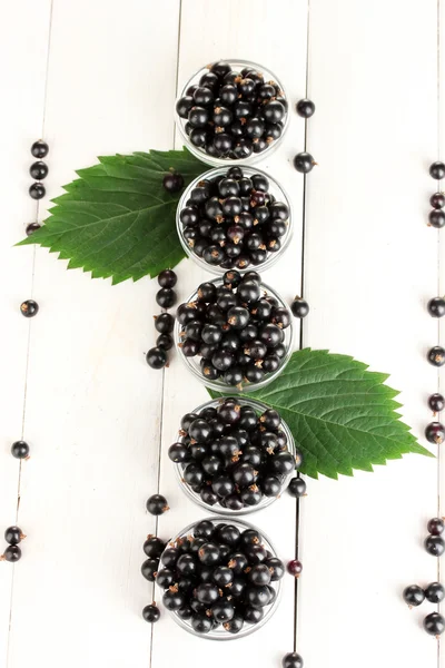 Fresh black currant in transparent bowls on white wooden background close-up — Stock Photo, Image