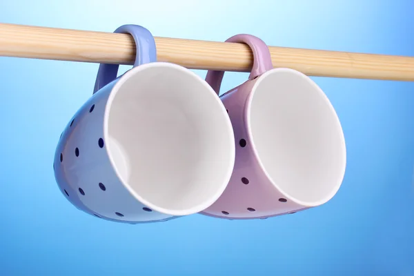 Schöne Tassen hängen auf Stick auf blauem Hintergrund — Stockfoto