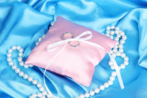 蓝色布料背景上的缎面枕上的结婚戒指 — 图库照片