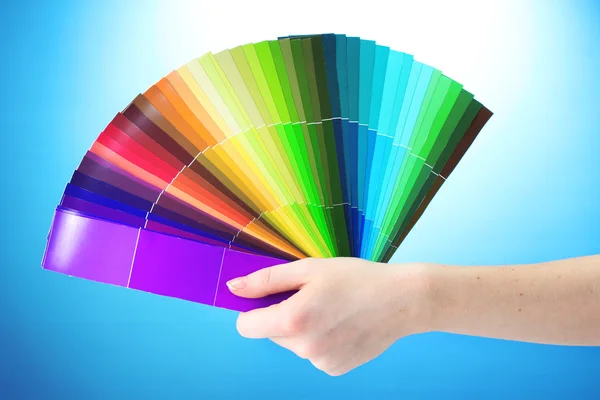 Ruka držící světlé palety barev na modrém pozadí — Stock fotografie