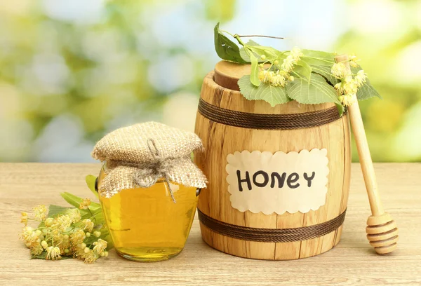 Баночка і бочка з липовим медом і квітами на дерев'яному столі на зеленому фоні — стокове фото