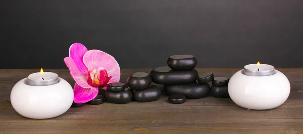 蘭の花とグレーの背景上の木製のテーブルの上のろうそくスパ石 — ストック写真