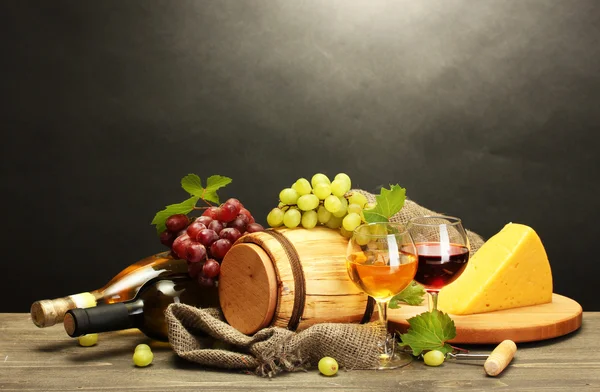 Barel, lahve a sklenice vína, sýrů a zralé hrozny na dřevěný stůl na šedém pozadí — Stock fotografie