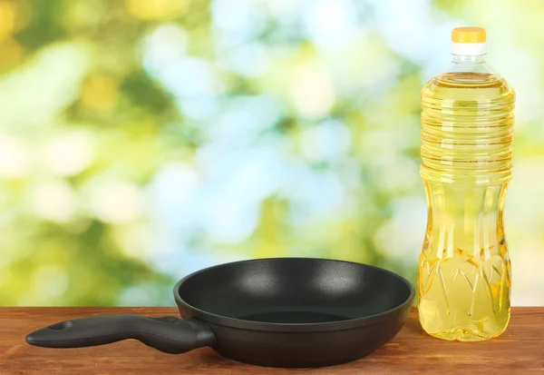 Pan with bottle of oil on wooden table — Stock Photo, Image