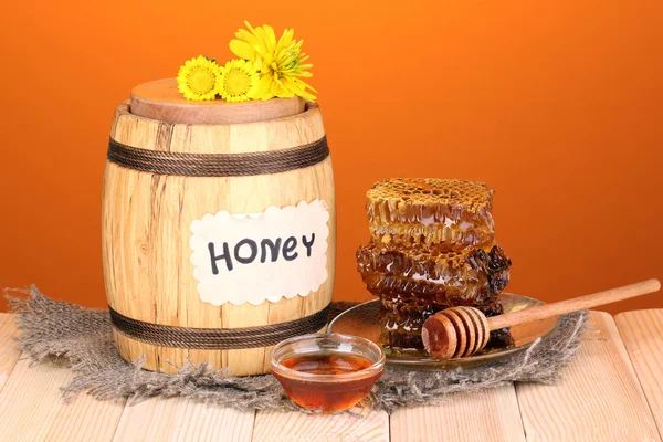 Cañón de miel y panal sobre mesa de madera sobre fondo naranja — Foto de Stock