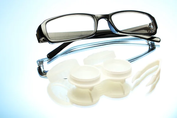 Gafas, lentes de contacto en recipientes y pinzas sobre fondo azul — Foto de Stock